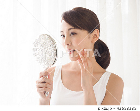 頬に手をあてて窓辺で鏡を見る女性 42653335