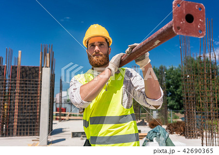Blue-collar worker carrying a heavy metallic bar during work 42690365