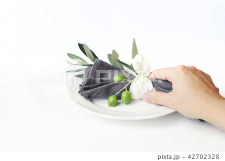 Woman hand holding grey linen napkin decoted by olive branch and silk ribbon. Festive table summer Woman hand holding grey linen napkin decoted by olive branch and silk ribbon. Festive table summer 42702328
