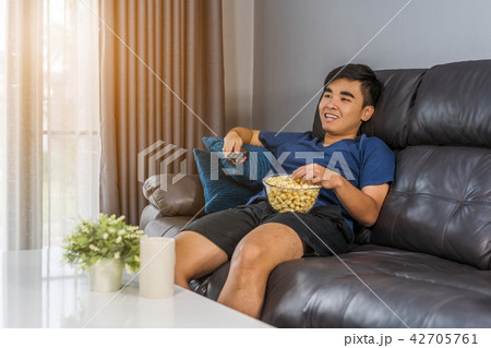 man eating popcorn while sitting on a couch at home and watching 42705761