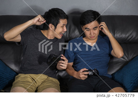 two man playing video games while sitting on sofa. win and lose two man playing video games while sitting on sofa. win and lose 42705779