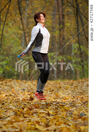 Photo of side view of sporty brunette jumping with rope at autumn forest 42717566