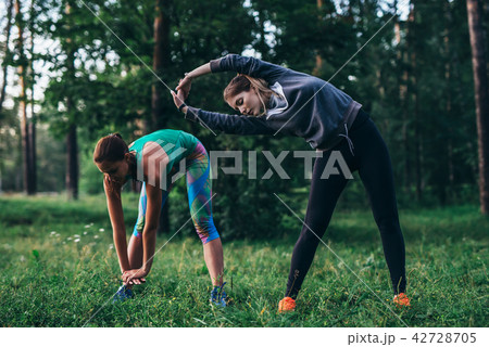 Two female runners doing warming-up bending exercises stretching back and leg muscles before running Two female runners doing warming-up bending exercises stretching back and leg muscles before running 42728705