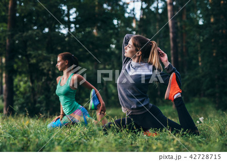 Girls sitting in one leg king pigeon pose during training session in yoga camp Girls sitting in one leg king pigeon pose during training session in yoga camp 42728715