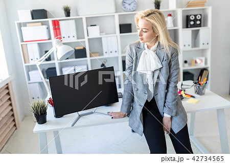 Young girl stands in office, leaning on desk. Nearby is a monitor. Young girl stands in office, leaning on desk. Nearby is a monitor. 42734565