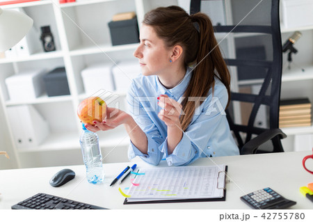 A young girl sits at a table in the office and holds an apple in her hand. A young girl sits at a table in the office and holds an apple in her hand. 42755780