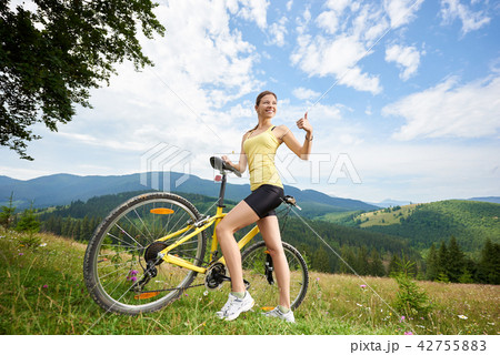Attractive female cyclist with yellow mountain bicycle, enjoying sunny day in the mountains 42755883