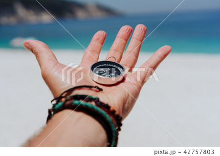 Outstretched hand holding black metal compass against white sandy beach and blue sea. Find your way 42757803
