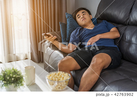 man holding remote control and watching TV while sitting on sofa 42763902
