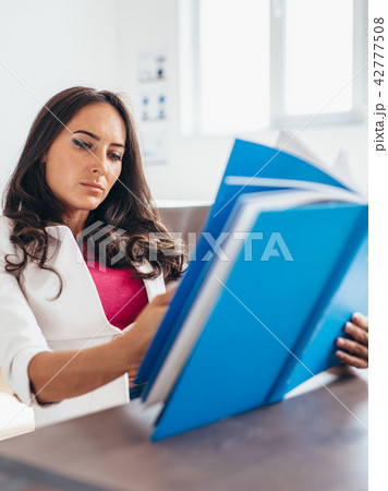Young woman sitting by table and reading book 42777508