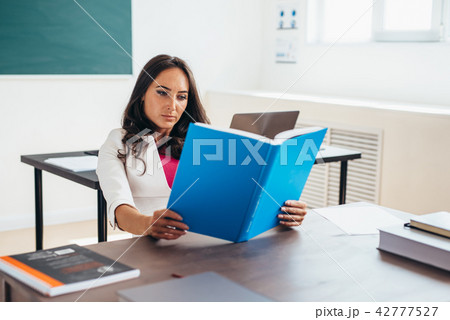 Young woman sitting by table and reading book. 42777527