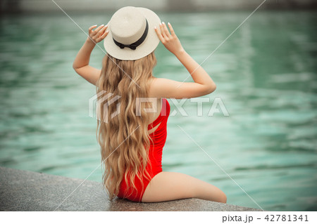 Pretty smiling girl is wearing red swimsuit resting near swimming pool with blue water. summer Pretty smiling girl is wearing red swimsuit resting near swimming pool with blue water. summer 42781341