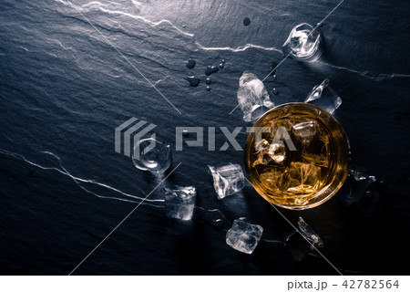 Glass of whiskey with ice cubes on dark table 42782564
