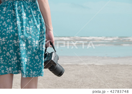 Woman in blue dress holding professional dslr camera on the beac Woman in blue dress holding professional dslr camera on the beac 42783748