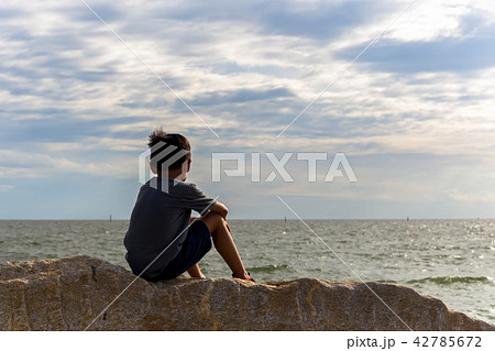 Boy sitting on rocks looking at the sea. Boy sitting on rocks looking at the sea. 42785672