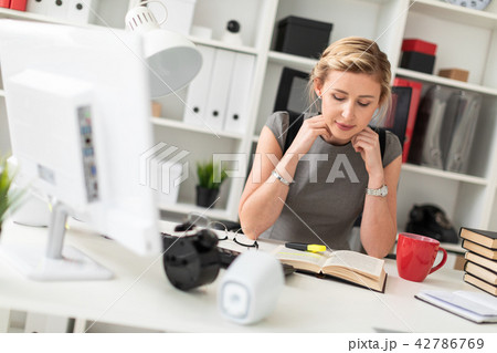 A young girl is sitting at a table in the office. Before the girl lies an open book. A young girl is sitting at a table in the office. Before the girl lies an open book. 42786769