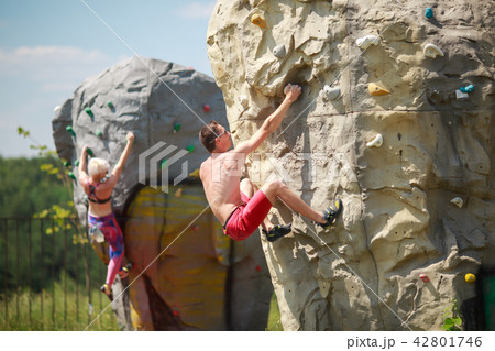 Photo of sports man in red shorts and woman on workout at climbing boulder against blue sky with 42801746