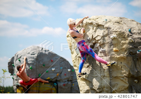 Photo of sports man and blonde in sunglasses climbing on boulders for rock climbing against blue sky 42801747