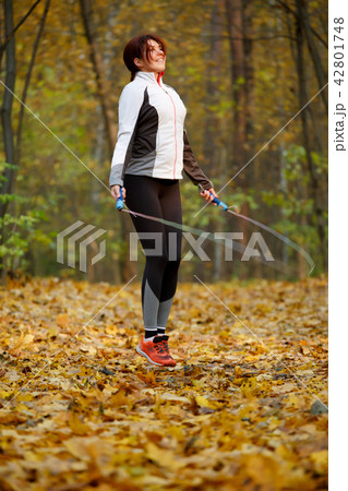 Picture of side view of sports girl jumping rope at autumn forest 42801748