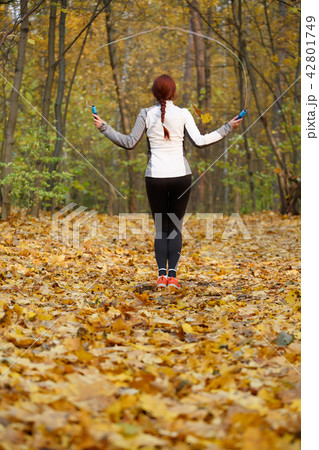 Photo from back of athlete girl jumping with rope at autumn forest Photo from back of athlete girl jumping with rope at autumn forest 42801749