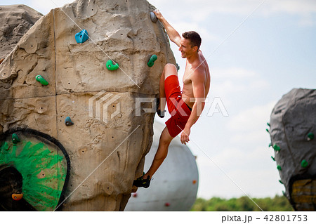 Photo of smiling guy in red shorts exercising on boulder for climbing against cloudy sky 42801753