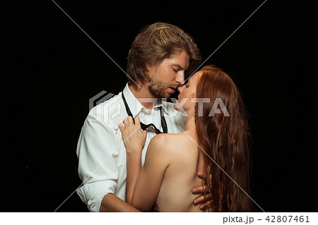 Real passion. Beautiful young loving couple bonding to each other while both standing against black Real passion. Beautiful young loving couple bonding to each other while both standing against black 42807461