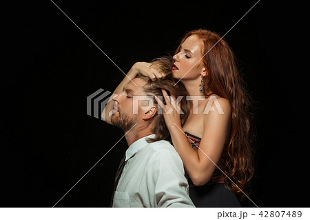 Real passion. Beautiful young loving couple bonding to each other while both standing against black 42807489