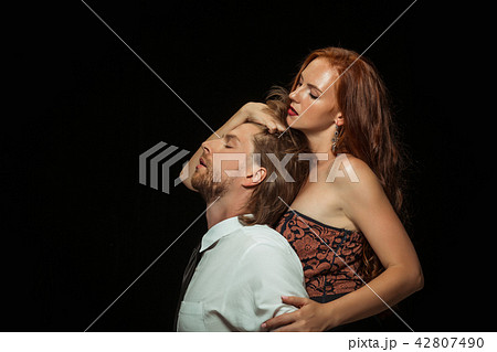 Real passion. Beautiful young loving couple bonding to each other while both standing against black Real passion. Beautiful young loving couple bonding to each other while both standing against black 42807490