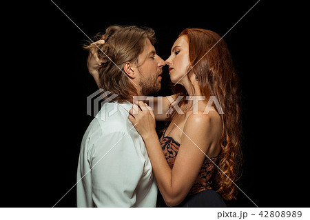 Real passion. Beautiful young loving couple bonding to each other while both standing against black Real passion. Beautiful young loving couple bonding to each other while both standing against black 42808989