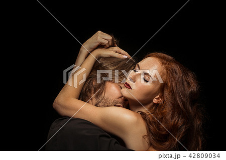 Real passion. Beautiful young loving couple bonding to each other while both standing against black 42809034