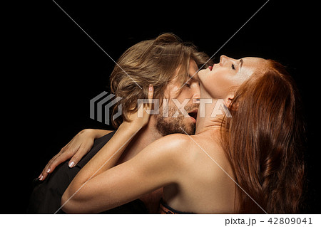 Real passion. Beautiful young loving couple bonding to each other while both standing against black 42809041
