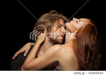 Real passion. Beautiful young loving couple bonding to each other while both standing against black 42809044