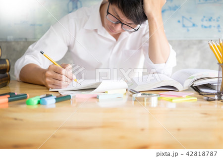teenage man sitting by wooden table reading and writting on note teenage man sitting by wooden table reading and writting on note 42818787