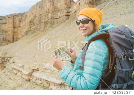 A traveler in a hat and sunglasses holds a hundred dollar bills in the hands of a fan against the A traveler in a hat and sunglasses holds a hundred dollar bills in the hands of a fan against the 42855257