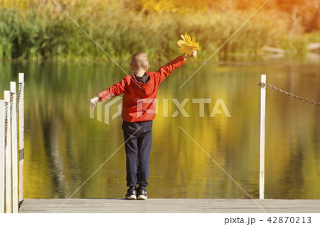 Boy in red jacket standing on the pier with leaves 42870213