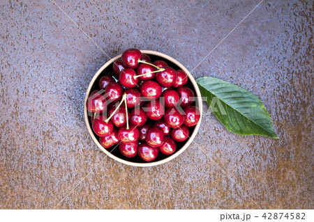 Fresh sweet cherries bowl with leaves on grunge rust background 42874582