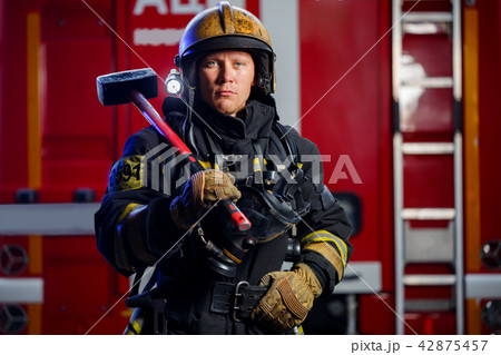 Photo of young fireman with sledgehammer in hands near fire engine 42875457