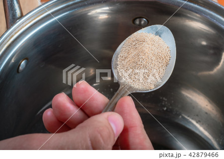 Female hand holds spoon with yeast over metal pan Female hand holds spoon with yeast over metal pan 42879466