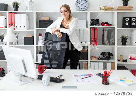 A young girl stands near a table in the office, with her hands on the chair. A young girl stands near a table in the office, with her hands on the chair. 42879755