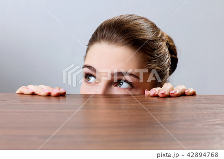 Woman peeping under the edge of wooden table 42894768