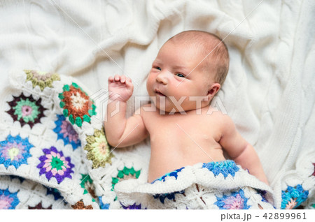 Newborn baby lying on bed, covered by a crocheted blanket. Top view. Newborn baby lying on bed, covered by a crocheted blanket. Top view. 42899961