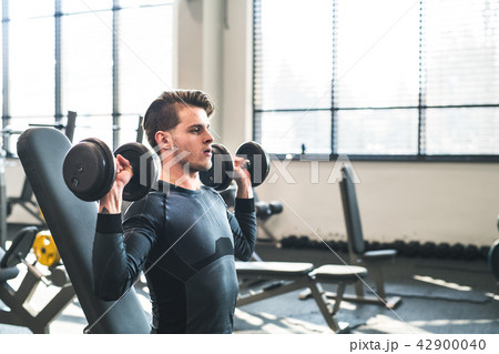 Young fit man in gym exercising with dumbbells. Copy space. 42900040