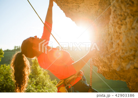 Photo of curly-haired female tourist clambering over rock 42903386