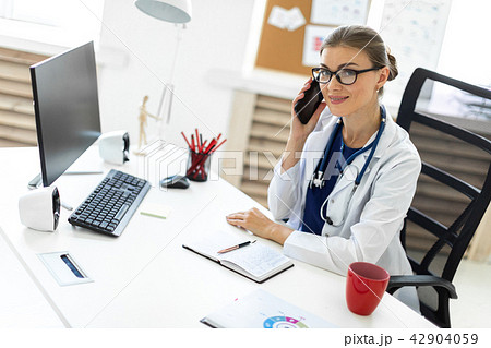 A young girl in a white robe is sitting at a table in the office and is talking on the phone. A A young girl in a white robe is sitting at a table in the office and is talking on the phone. A 42904059