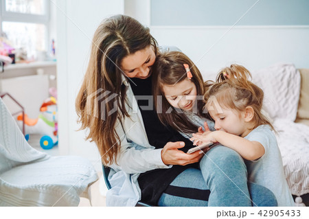Mom and two daughters are looking at the smartphone Mom and two daughters are looking at the smartphone 42905433