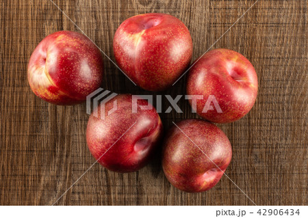 Fresh pluot interspecific plums on brown wood Fresh pluot interspecific plums on brown wood 42906434