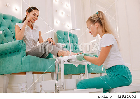 Dark-haired woman sitting in comfortable armchair getting pedicure 42921603
