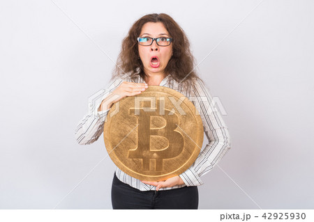 Surprised businesswoman with opened mouth looking camera and holding big golden bitcoin on white Surprised businesswoman with opened mouth looking camera and holding big golden bitcoin on white 42925930