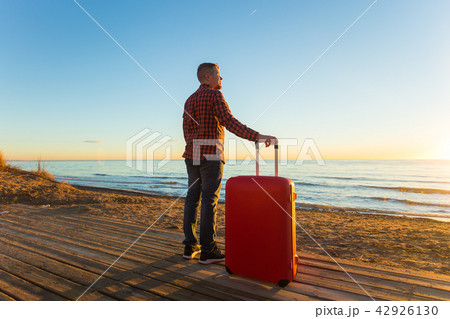 Nature, travel, people concept - a man standing near the sea with red suitcase Nature, travel, people concept - a man standing near the sea with red suitcase 42926130