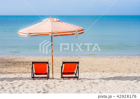 Two red wooden chairs and beach umbrella. 42928176